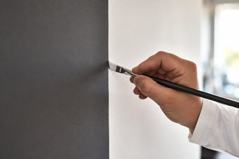 Mano de pintor profesional trazando con precisión una línea recta entre dos colores con pincel fino