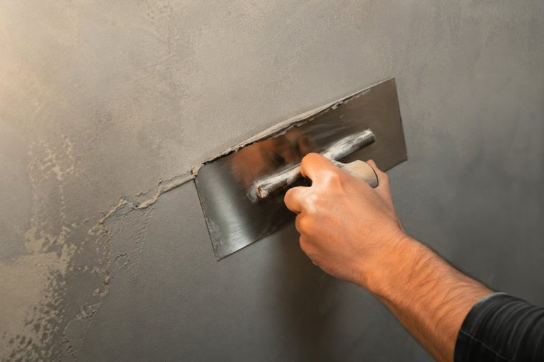 Aplicador profesional extendiendo microcemento gris con llana japonesa sobre una pared
